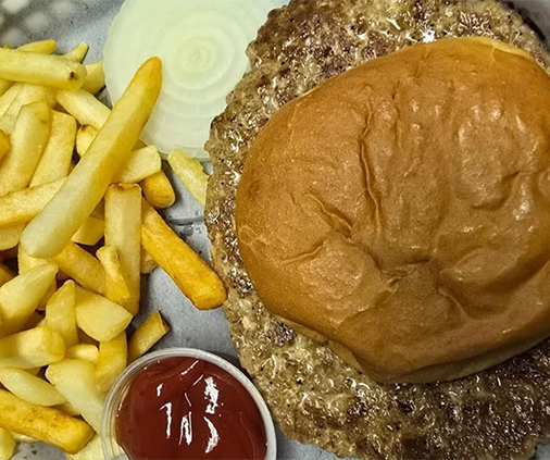 A burger on a brioche bun with french fries, a slice of raw onion and a cup of ketchup